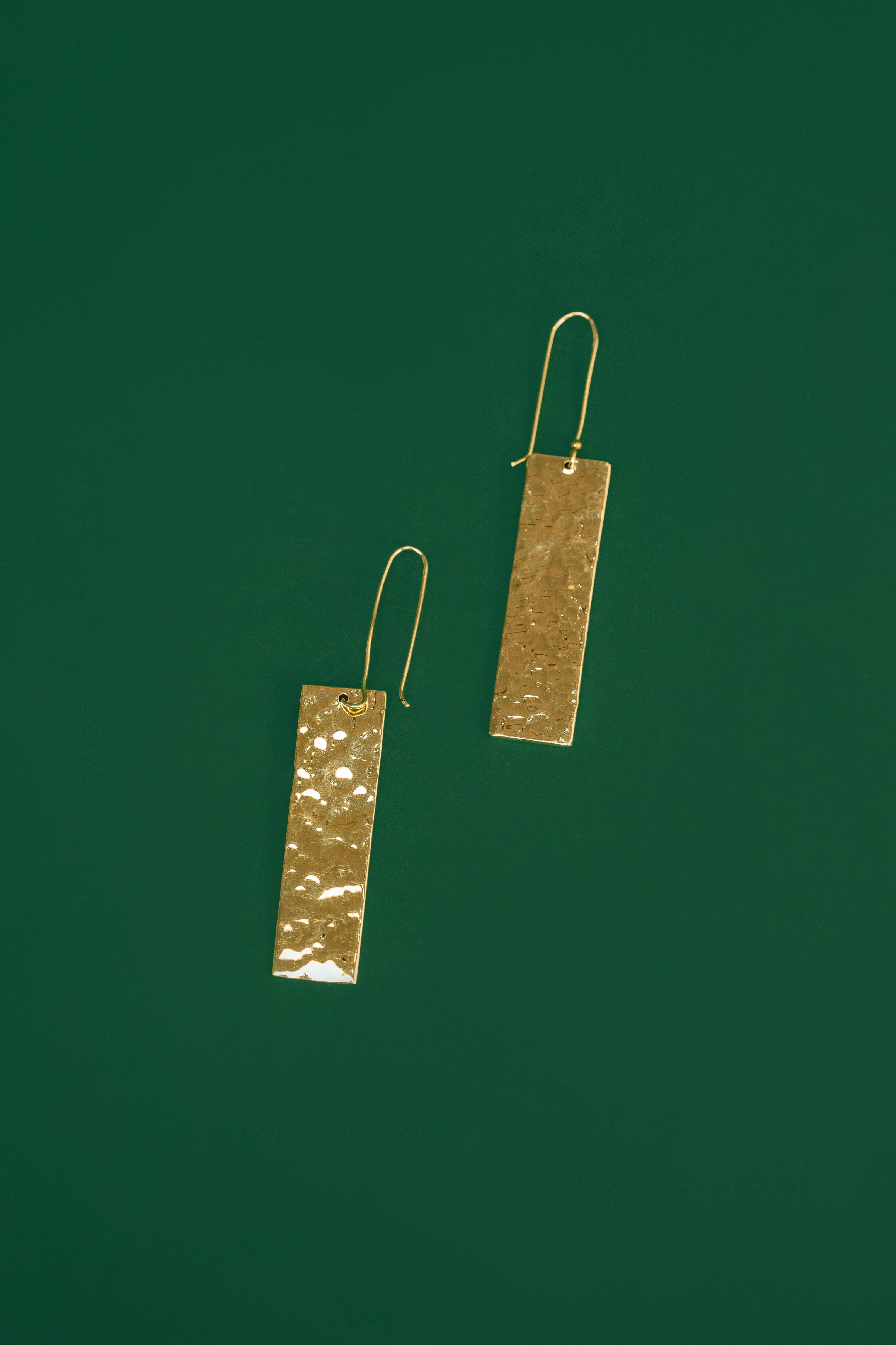 Pair of gold rectangular earrings on a green background