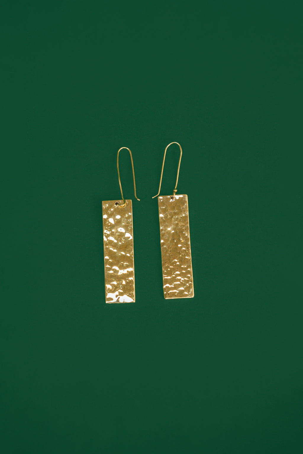 Gold rectangular earrings on a dark green background