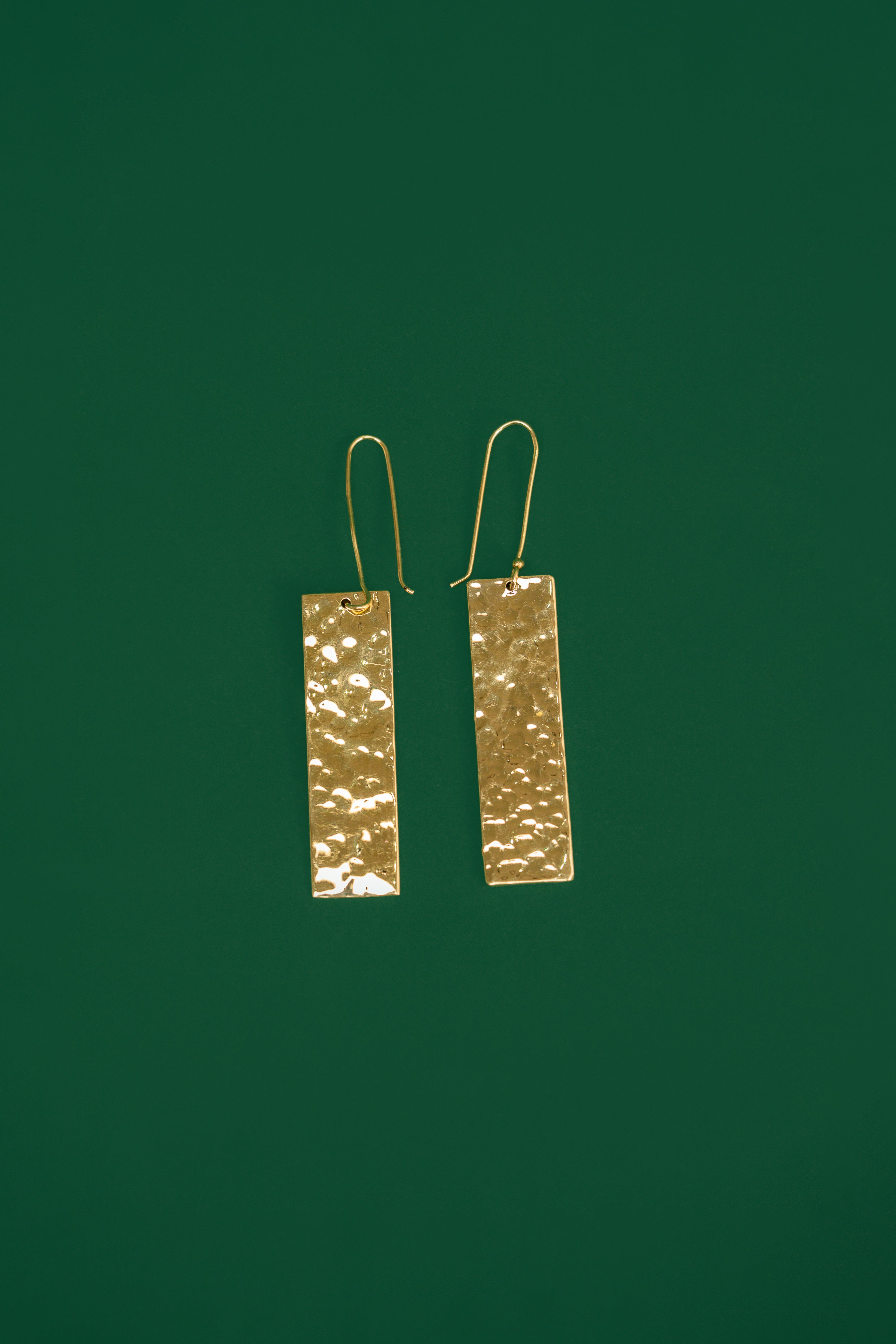 Gold rectangular earrings on a dark green background