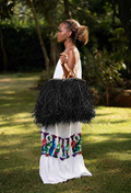 Model in a white dress holding a statement bag with black colored raffia strands covering the basket and wooden handles