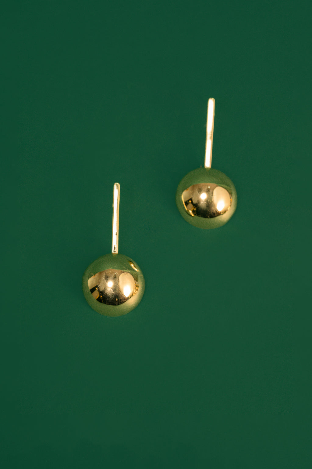 Pair of gold spherical drop earrings on a green background