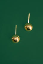 Pair of gold spherical drop earrings on a green background