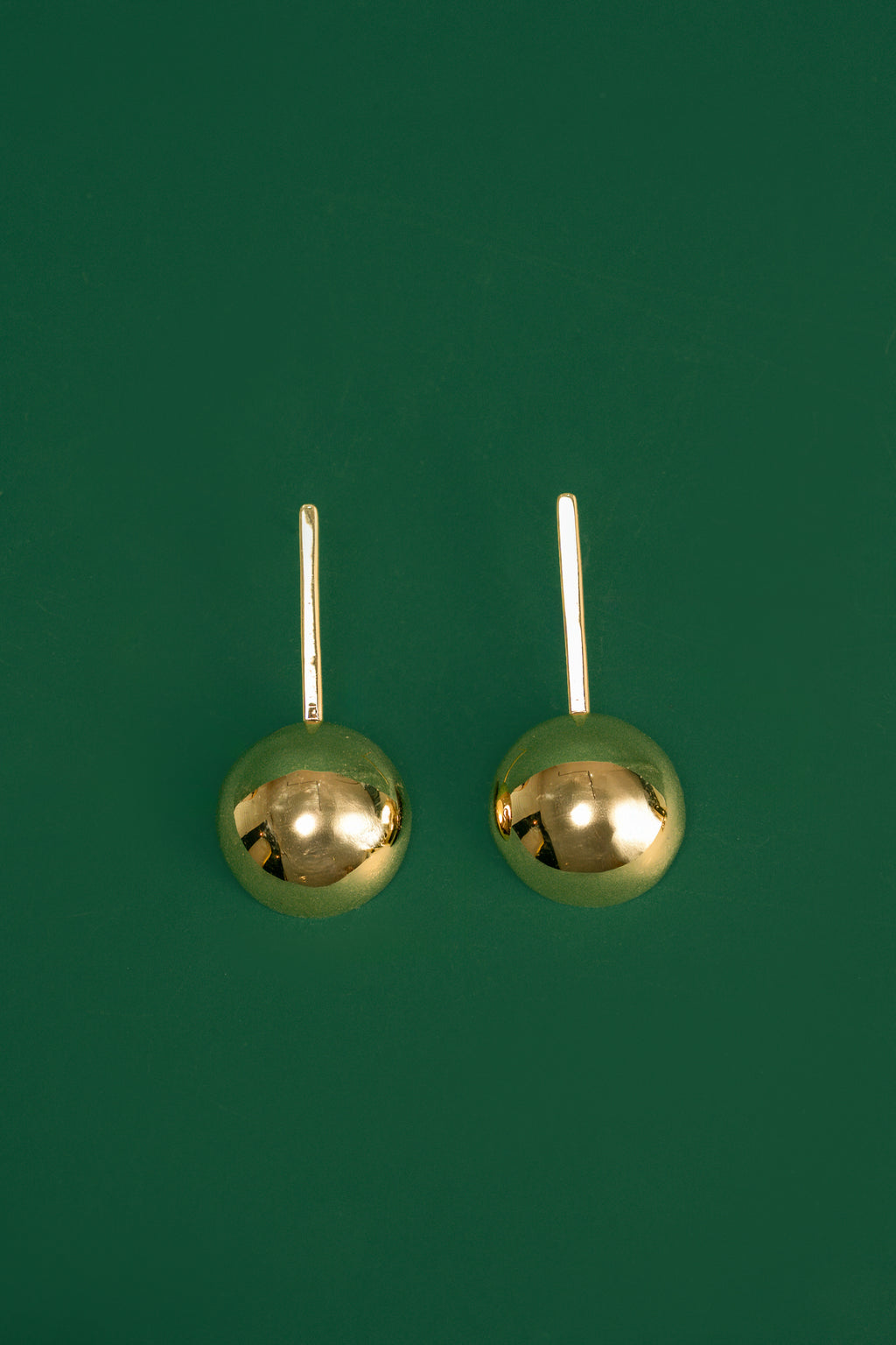 Pair of gold spherical drop earrings on a green background