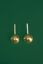 Pair of gold spherical drop earrings on a green background