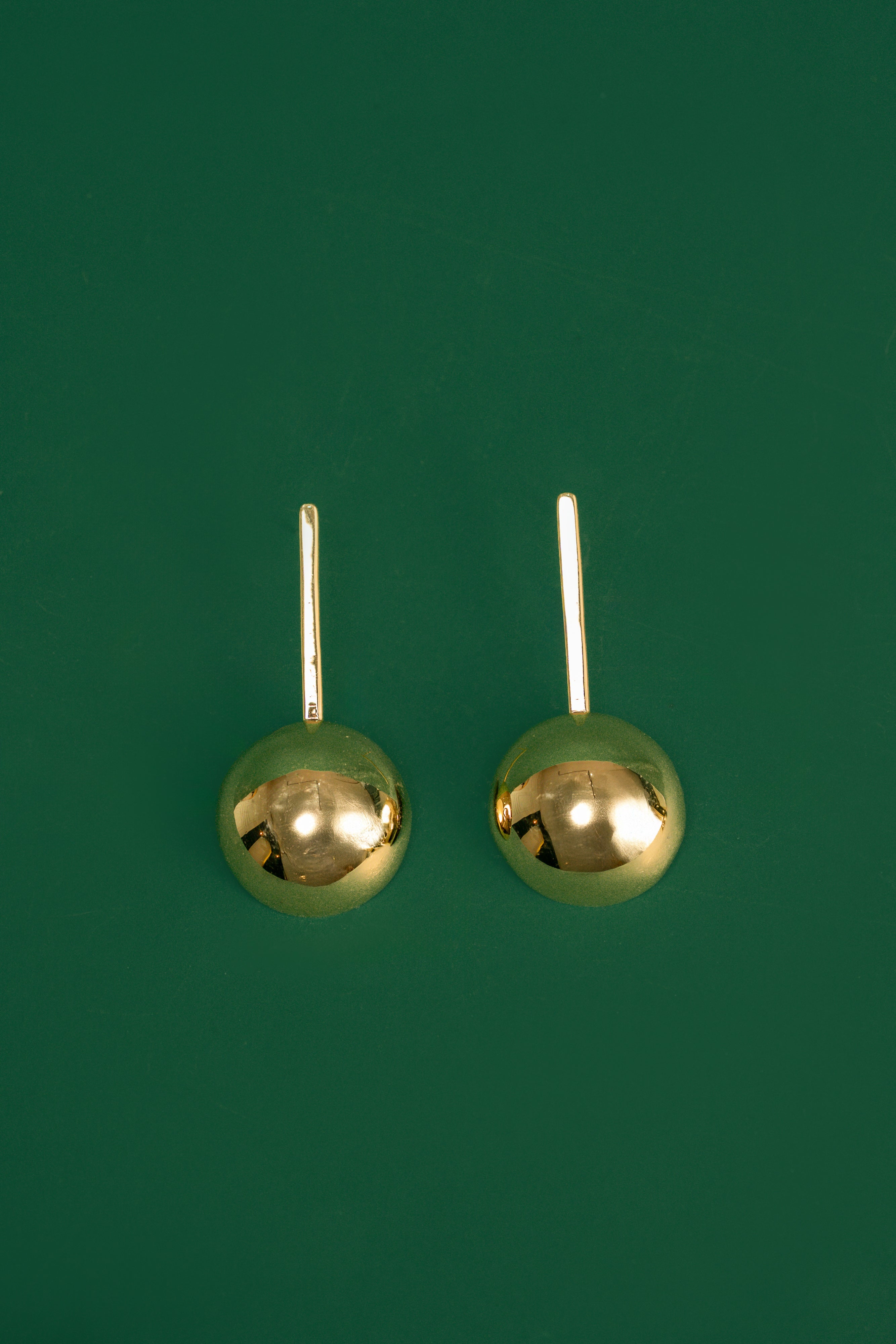 Pair of gold spherical drop earrings on a green background