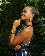 Model wearing gold rectangular with a brown circle pendant earrings and a brown cow horn circular cuff bracelet.