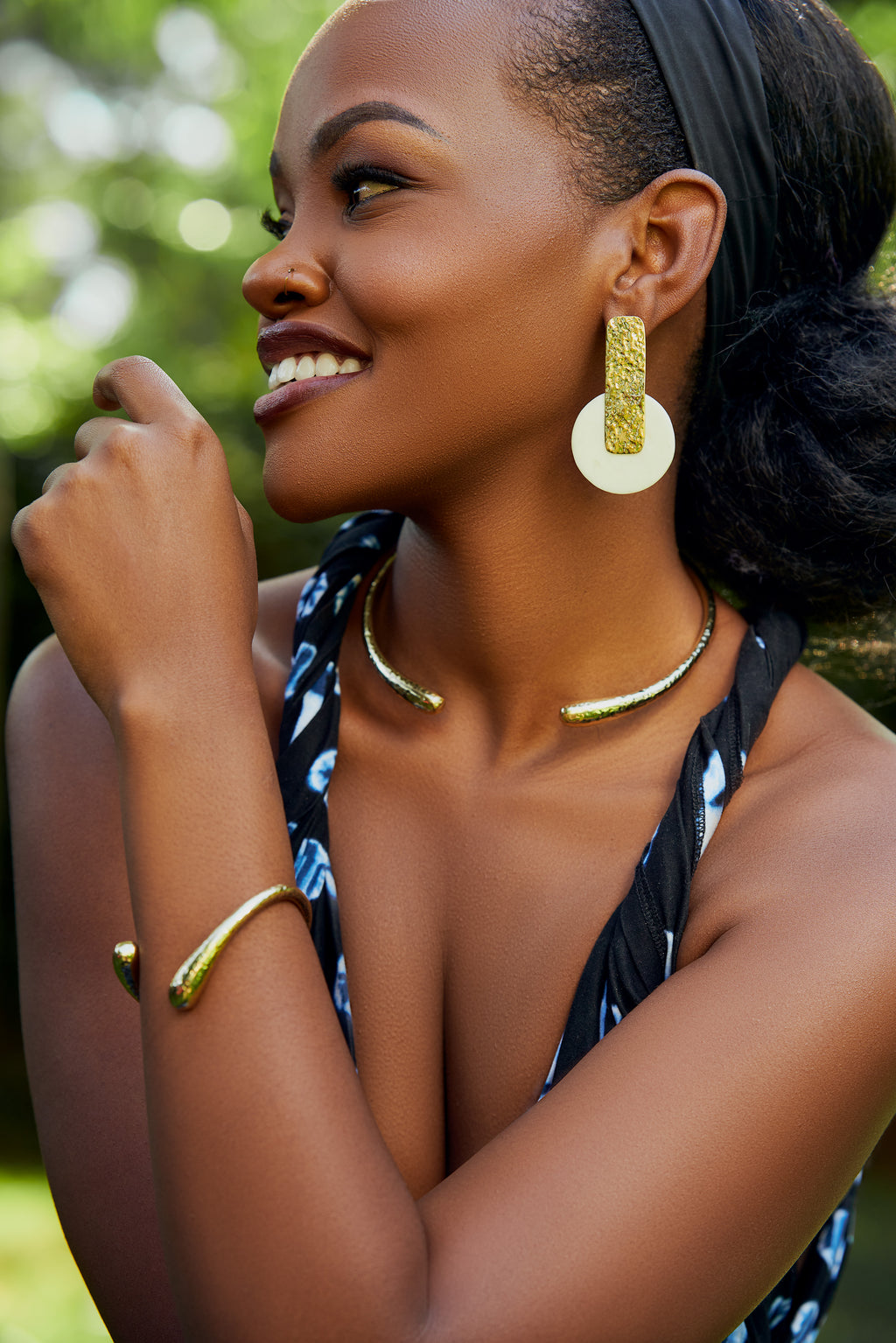 Model wearing gold rectangular with a white circle pendant earrings, a twisted gold bracelet and a gold choker.