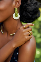 Close-up of a model wearing gold rectangular with a white circle pendant earrings, two twisted gold rings and a gold choker.