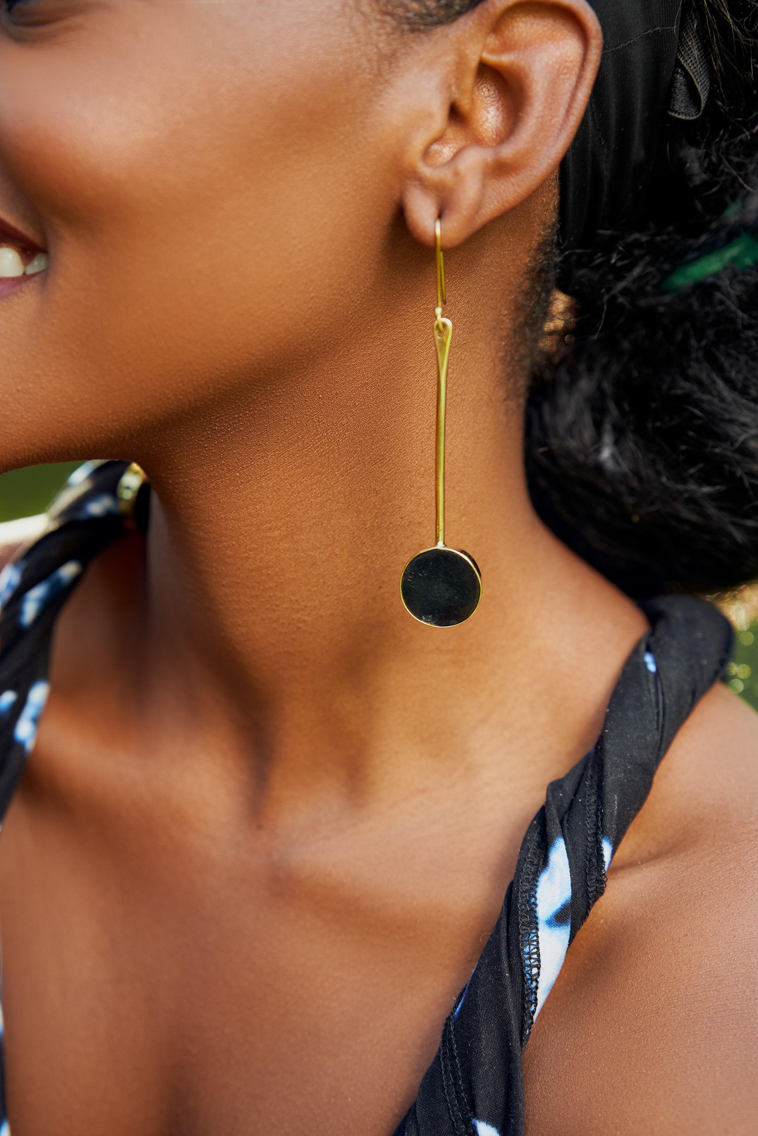 Model wearing a drop long bar gold earrings and a black circular end 